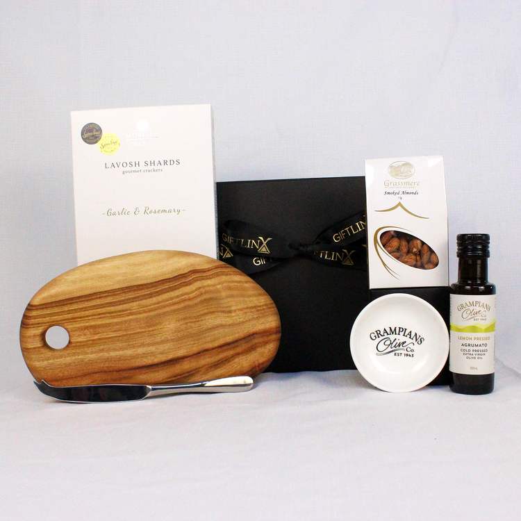 Black magnetic gift box with ribbon surrounded by the products to be included such as a small handmade timber cheese board with stainless steel cheese knife, lavosh shards, smoked almonds and an infused olive oil with dipping bowl.