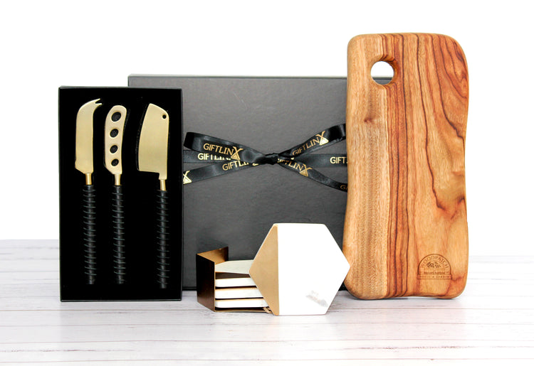 Black gift box with ribbon housing a handmade cheese board, brass and leather cheese knife set and a set of marble and brass coasters.