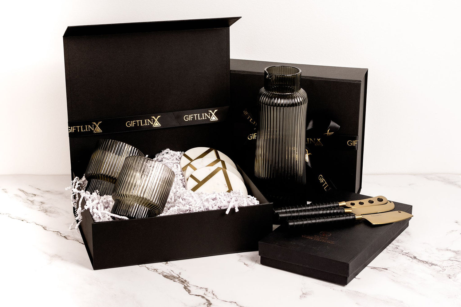 black gift box housing brass and marble coasters and ribbed glass tumblers. A ribbed glass carafe stand next to it
