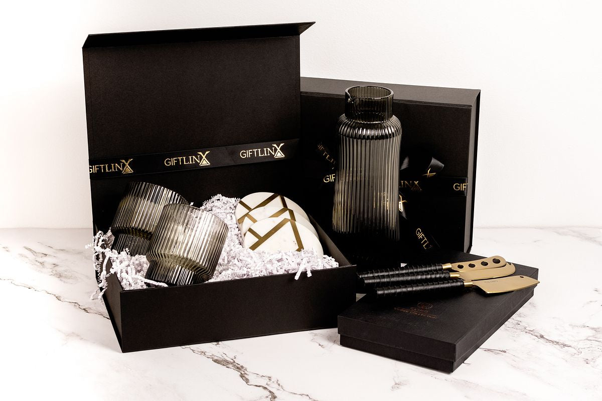 Black and gold gift boxes with brass, marble and leather accessories for cheese boards, ribbed glass carafe with matching glassware