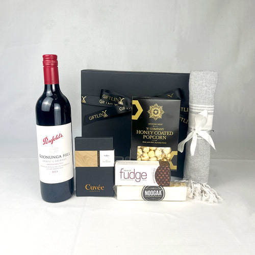 Gift basket with Penfolds wine, popcorn, fudge, and a blanket on a white background