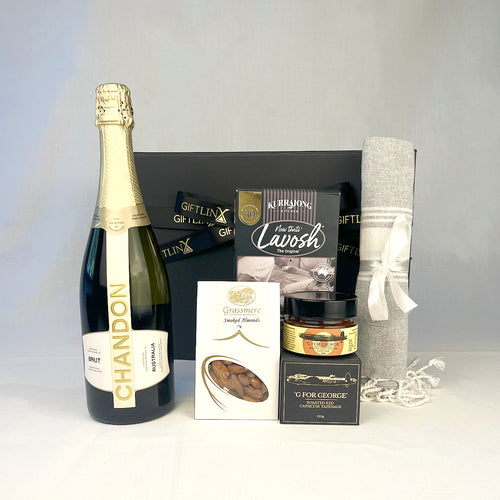 Gift basket with Chandon champagne, Lavosh crackers, and other items on a gray background