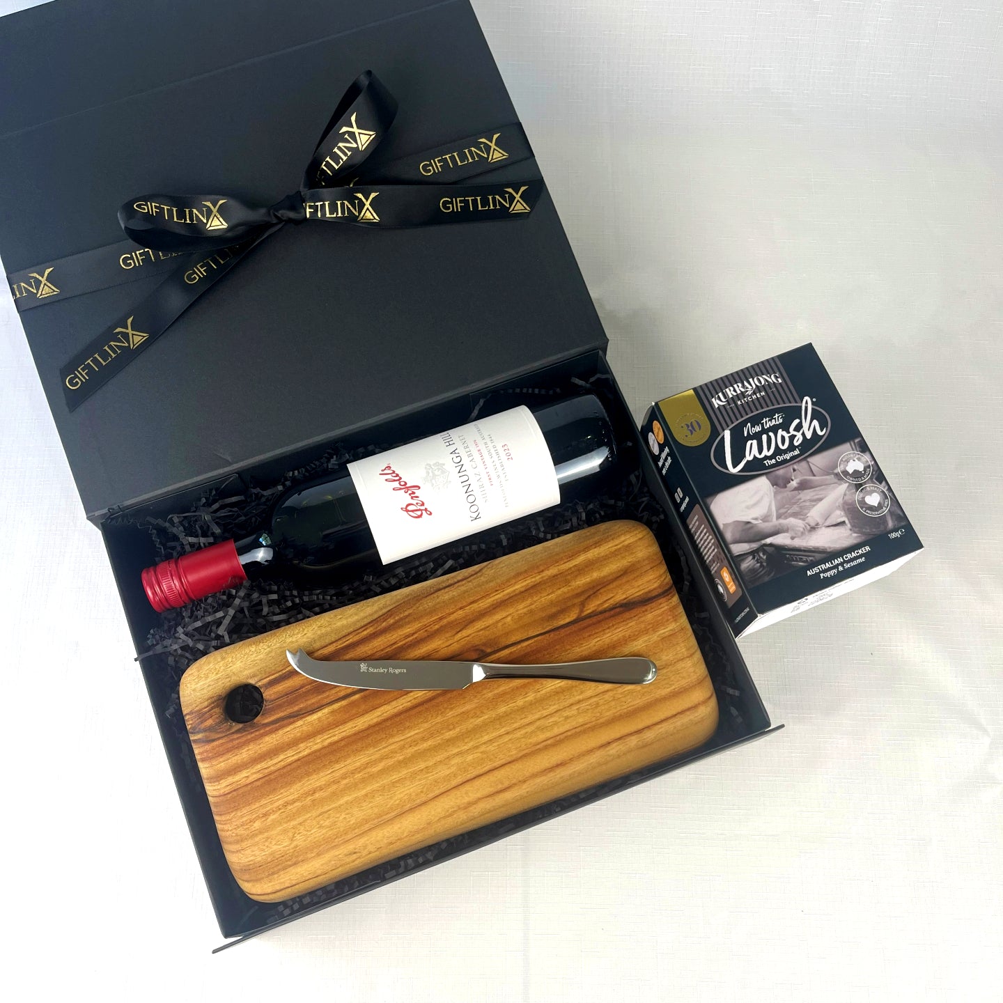 Gift set with wine bottle, cutting board, and knife in a black box labeled 'GIFTLINX'.