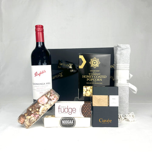 Gourmet gift basket with wine, popcorn, and other treats on a white background