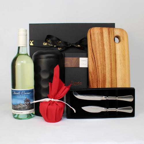 Bottle of Devils Corner white wine next to a black stainless steel wine cooler, block of chocolate, a timber serving board, cheese knife set and a small Christmas pudding