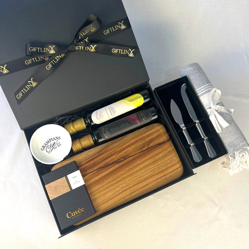 Gift set with bottles, wooden board, and cutlery in a black box labeled 'GIFTLINX'.