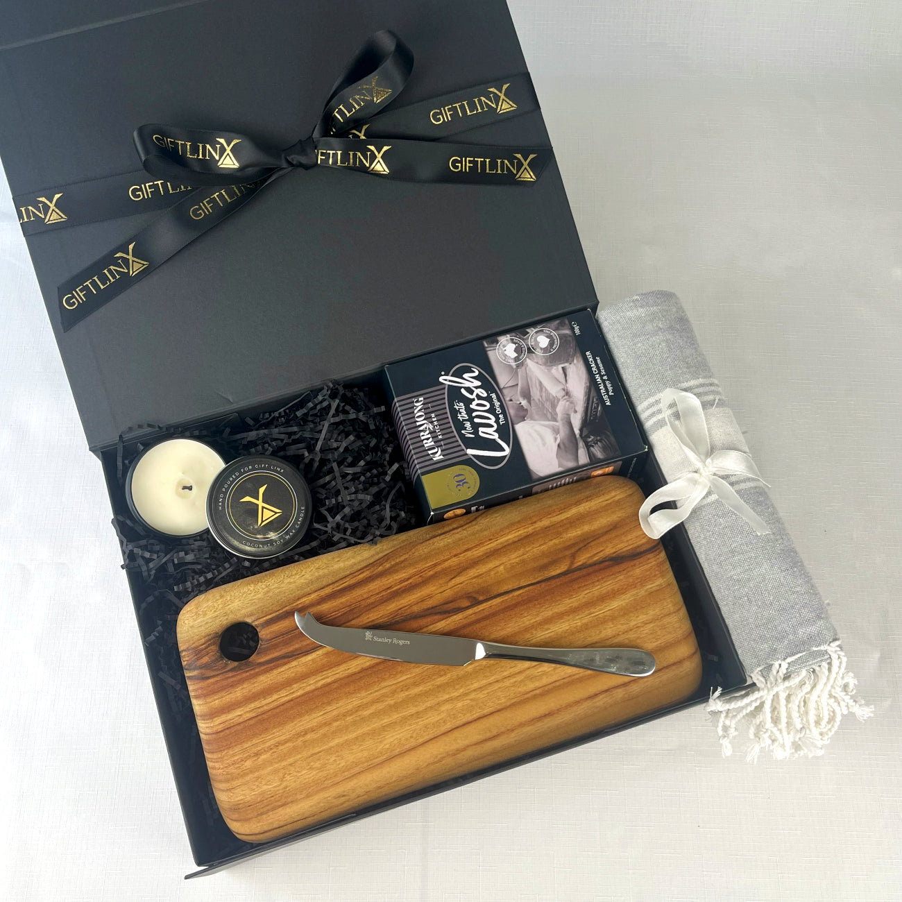 Gift set with wooden cutting board, knife, candle, and other items in a black box labeled 'GIFTLINX'.