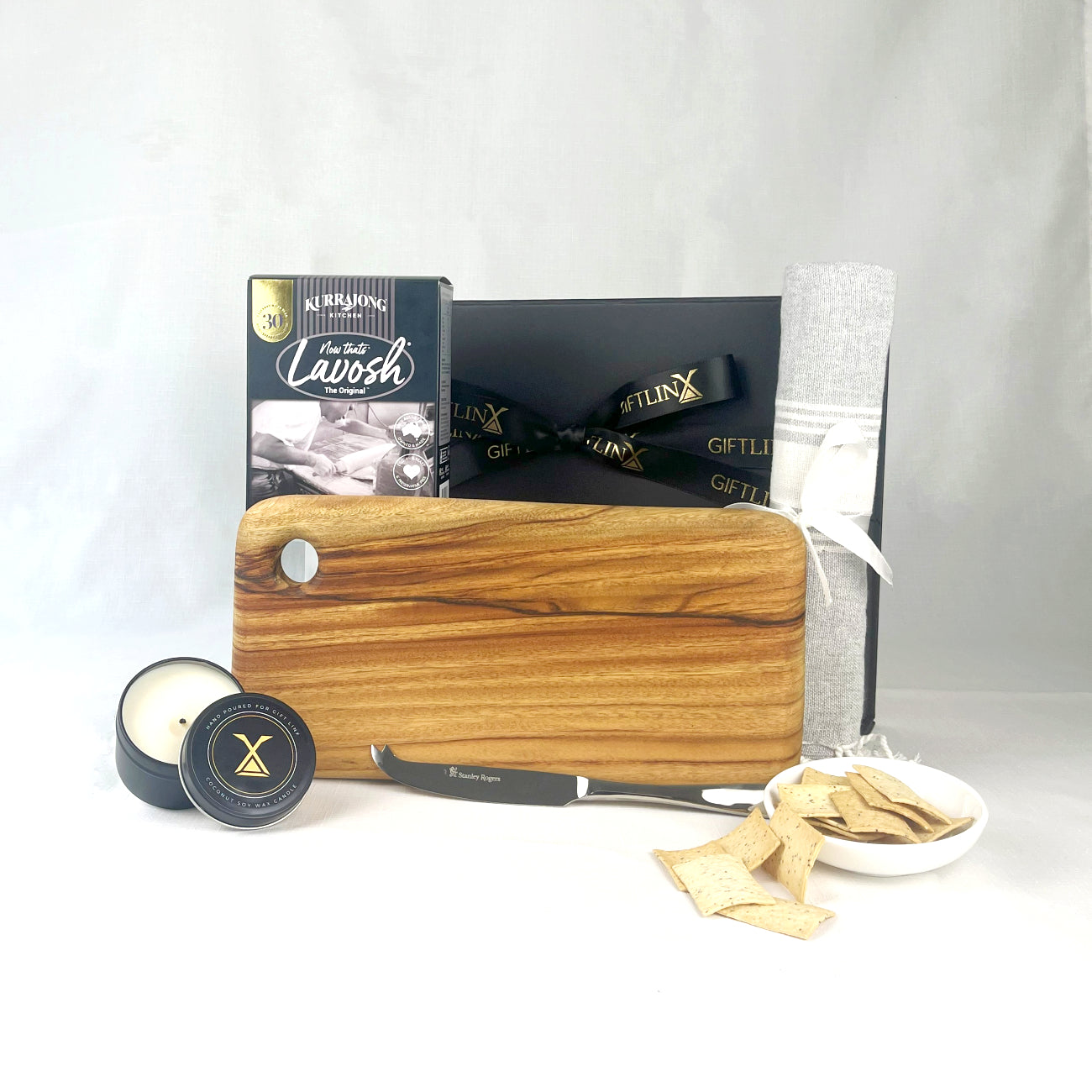 Wooden cutting board with a knife, candle, and small bowl of chips on a white background