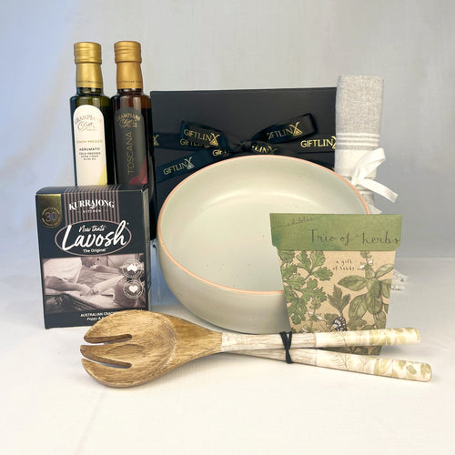 Gourmet gift set with olive oil, cheese, and kitchen utensils on a white background