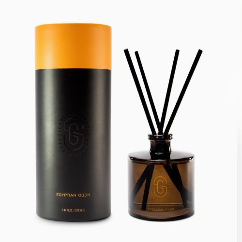 a black and gold presentation tube next to a glass jar of home diffuser with reeds