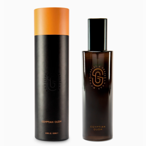 room spray in a dark glass bottle with black lid standing next to black and gold presentation tube with white background