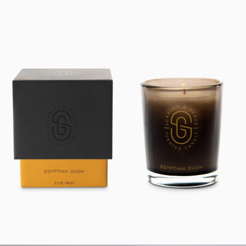 small glass candle, lit, next to black and gold box on white background