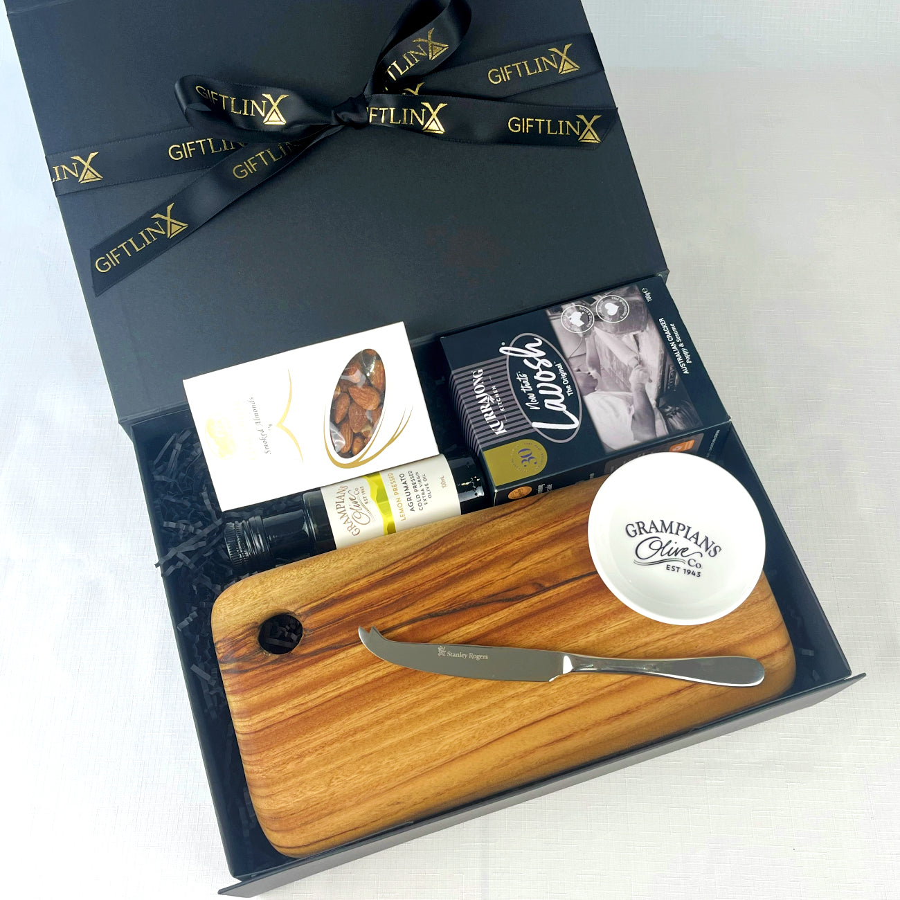 Gift set with wooden cutting board, knife, and bottle of olive oil in a black gift box.