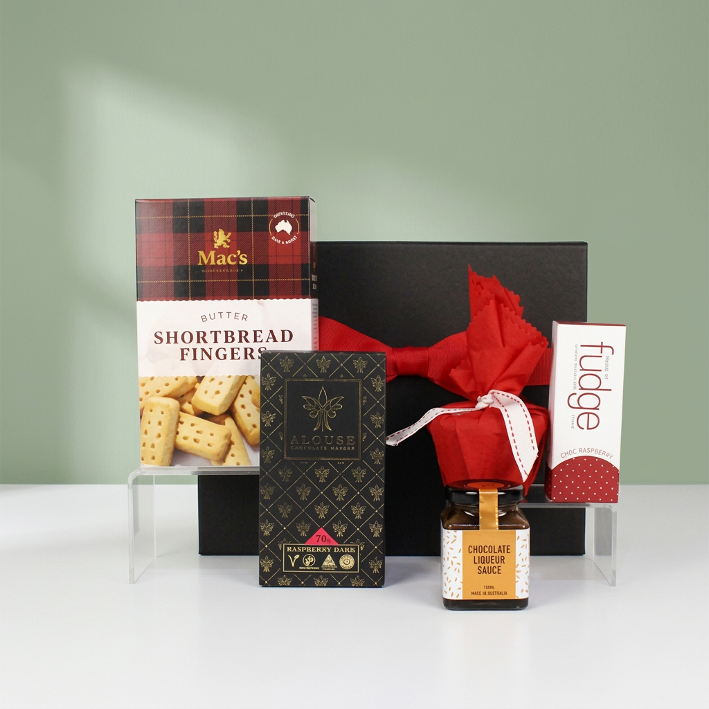 black gift box with red ribbon behind Australian made shortbread fingers, chocolate, Christmas pudding, pudding sauce and fudge bar