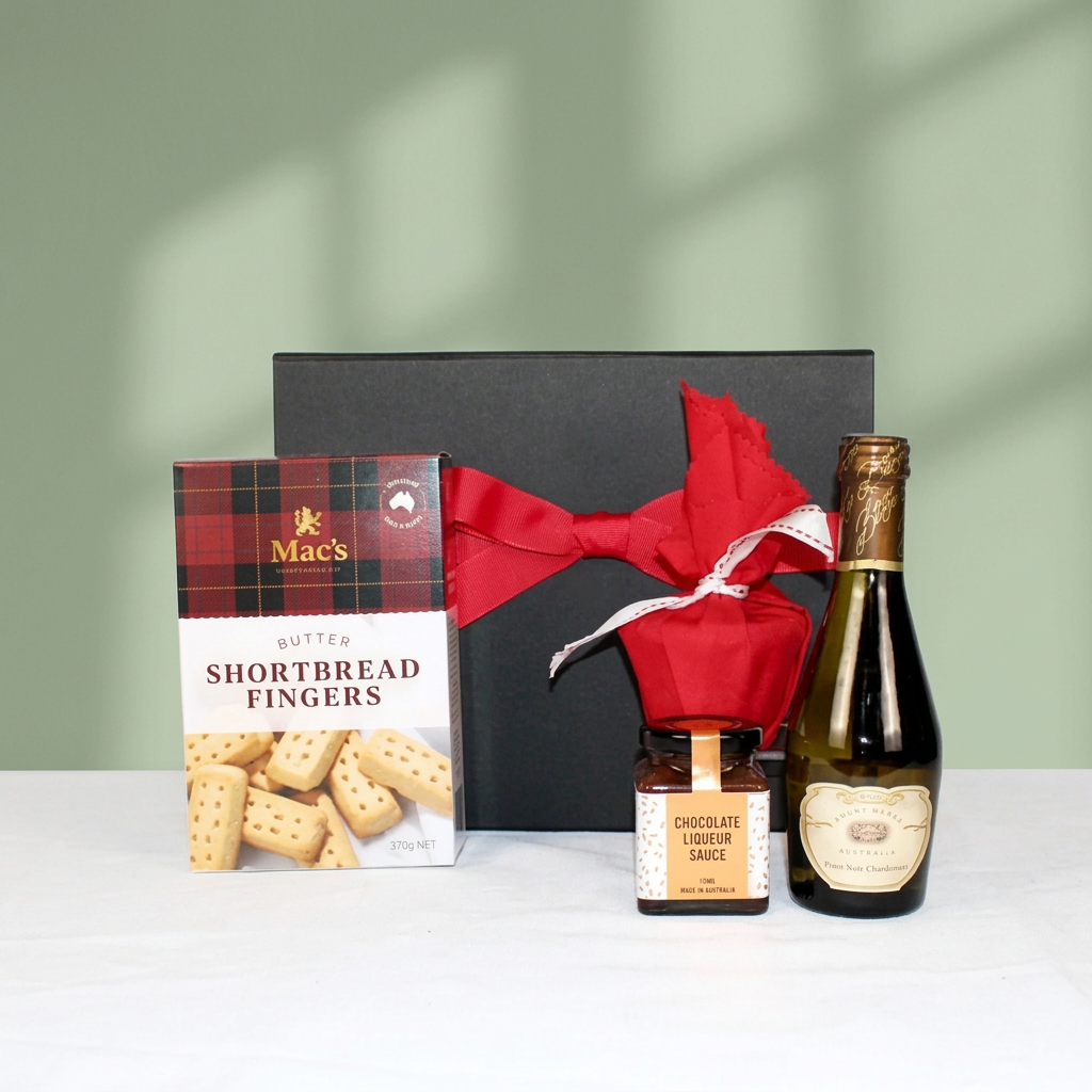 black gift box with red ribbon behind Australian made shortbread, Christmas pudding, pudding sauce and a piccolo of sparkling wine