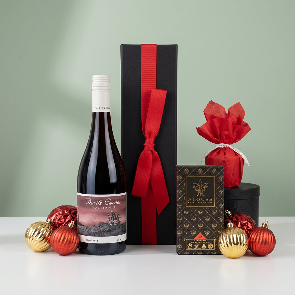 black gift box with red ribbon next to a bottle of Australian wine accompanied by Chocolate and Christmas pudding surrounded by tree baubles