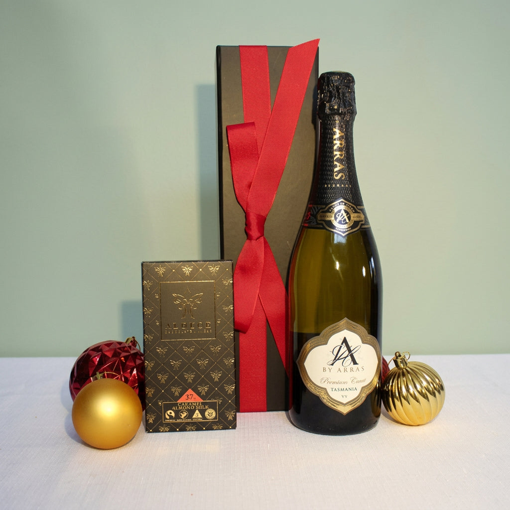 black gift box with red ribbon behind a bottle of Australian sparkling wine and handmade chocolate surrounded by Christmas baubles
