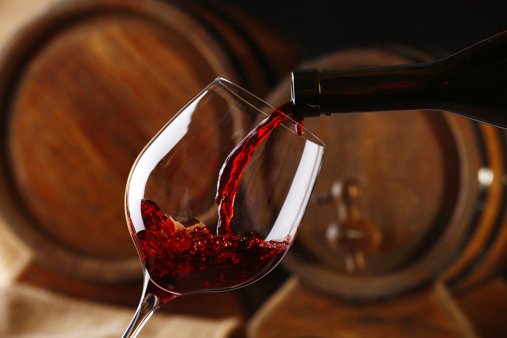 Red wine being poured into a glass with wine barrels in the background