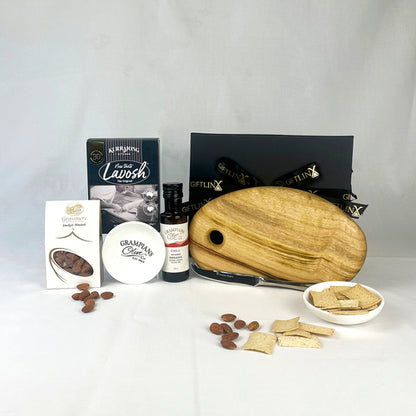Assorted snacks and items including a wooden cutting board, crackers, and a bottle of sauce on a white background.