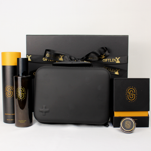 Black gift box standing behind a moulded black case with first aid kit, a black and gold box with a car diffuser laying in front and a glass black jar with black presentation tube
