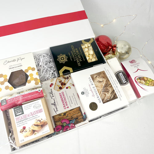 Assorted chocolate bars and treats in a box with red ribbons on a white surface