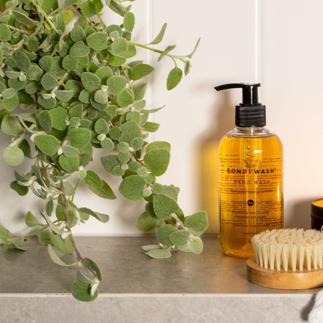 Beautifully set Bondi Wash Hand wash on stone bathroom shelf with timber brush and greenery.