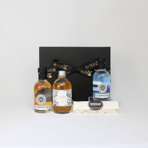 Black gift box standing behind two bottle of gin and a bottle of lime syrup alongside a bar of nougat