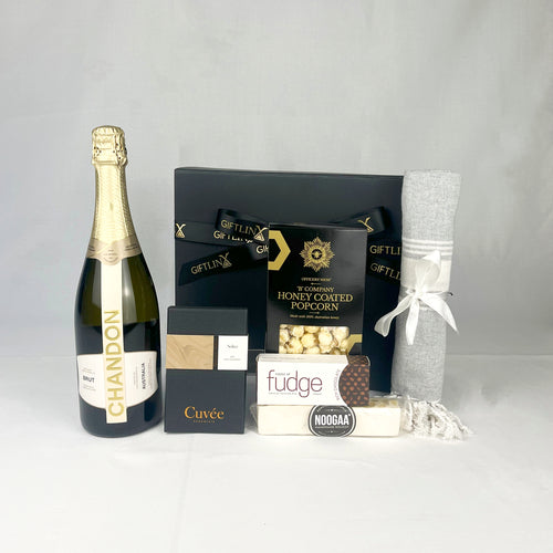 Gift basket with Chandon champagne, popcorn, fudge, and a towel on a white background