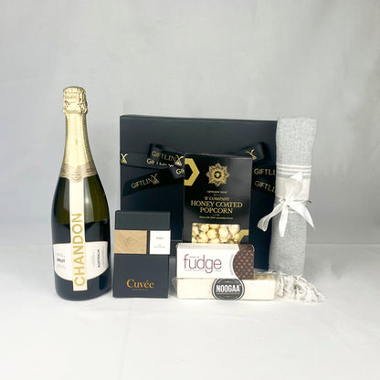 Gift basket with Chandon champagne, popcorn, fudge, and a towel on a white background