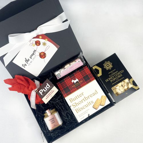 Gift box with butter shortbread biscuits, honey coated popcorn, and other treats on a white background