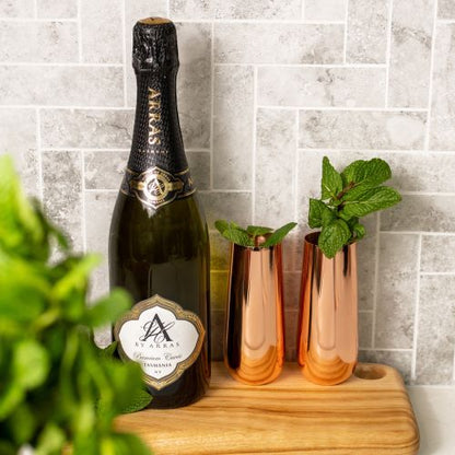 pair of copper stemless champagne flutes standing on a timber tray with a bottle of sparkling wine next to them