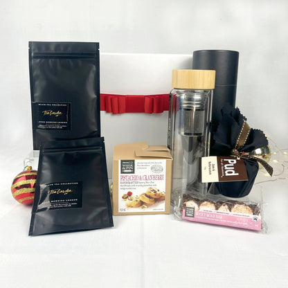 Collection of gift items including tea packages, a flask, and a box of shortbread and chocolate on a white background