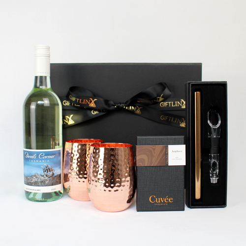 black gift box standing behind with a bottle of white wine, a pair of hammered copper glasses and a copper wine chilling stick and a block of chocolate