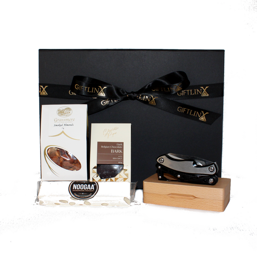 black gift box standing behind a multi tool on its timber case next to a bar of nougat, chocolate and smoked almonds in white packaging