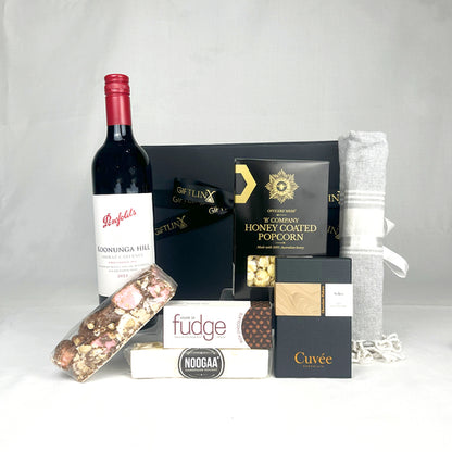 Gourmet gift basket with wine, popcorn, and other treats on a white background