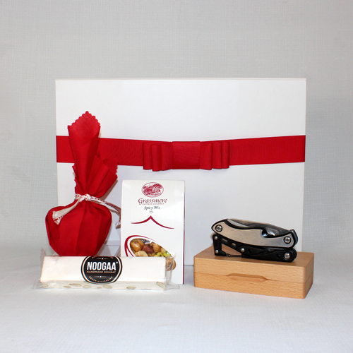 white gift box with red ribbon behind a multitool with timber case, nougat bar, Christmas pudding and nut mix next to