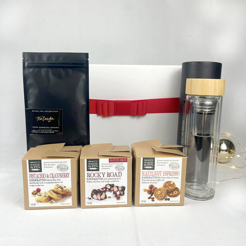 Assorted food products including a black tea sachet, a clear glass flask with a bamboo lid, and three boxes of chocolate  and cookies on a white background.