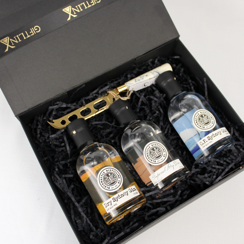 black gift box open with 3 small bottles of gin inside alongside a marble handled cheese knife