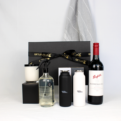 Black gift box with black and gold ribbon surrounded by a bottle of Australian wine, a pair of salt and pepper mills in black and white, a hand poured soy candle jar, a kitchen bench spray made with Australian botanicals and a 100% cotton hand towel in grey