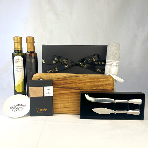 Gourmet gift set with olive oil, cheese boards, and knives on a white background