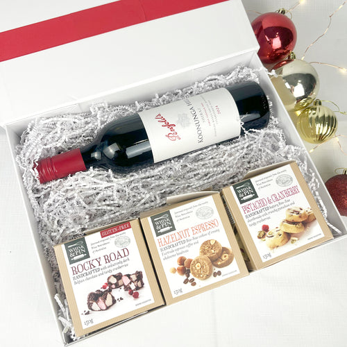 Wine gift set with a bottle of wine and three boxes of cookies and rocky road in a decorative box.