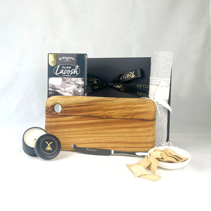 Wooden cutting board with a knife, candle, and small bowl of chips on a white background