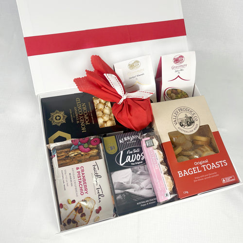 Gift box with assorted food products including bagel toasts and chocolate bars on a white background