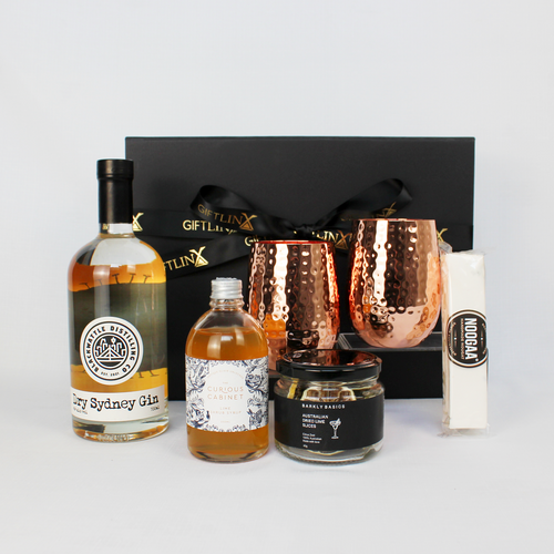black gift box standing behind a bottle of Australian gin, lime syrup with dried lime slices and copper drinkware