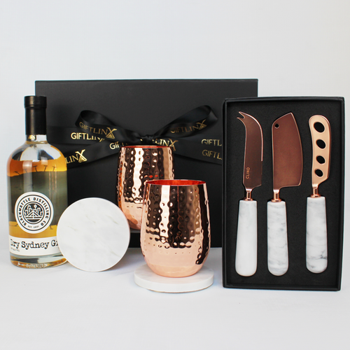 black gift box standing behind a bottle of Australian gin, a pair of copper stemless glasses on marble coasters next to a three piece cheese knife set with marble handles in a black gift box