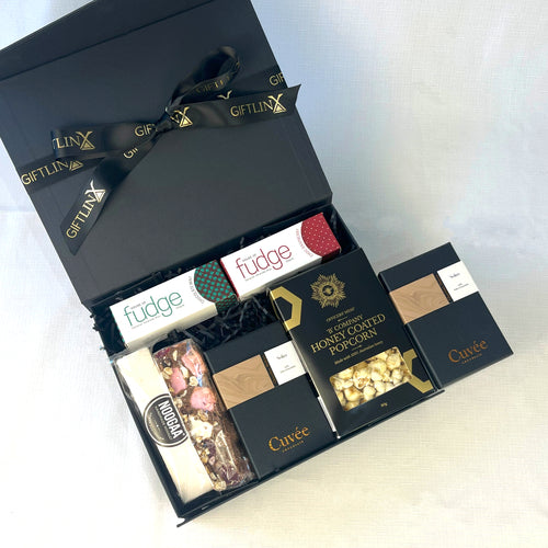 Open black gift box with various chocolate bars and popcorn on a white background