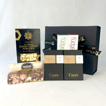 Gourmet gift basket with various treats including honey-coated popcorn, fudge, and chocolate bars on a white background.