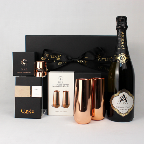 black gift box standing behind a bottle of Australian sparkling win, copper stemless champagne flutes and copper stopper with a block of chocolate