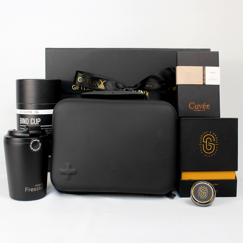 black gift  box standing behind a black moulded first aid kit, travel mug, chocolate and a care diffuser with black and gold box