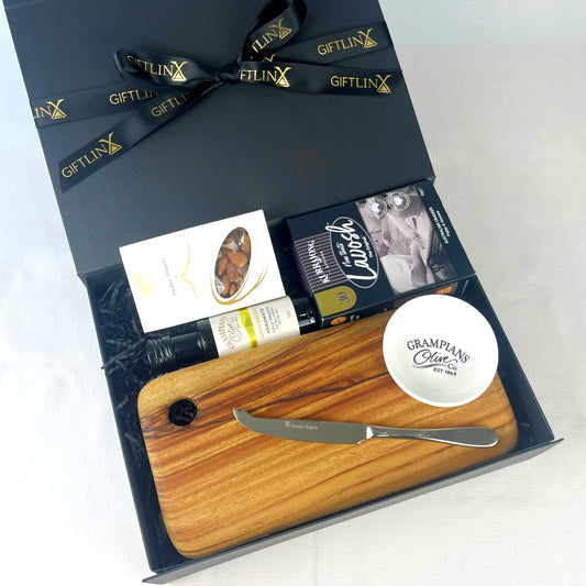 Gift set with wooden cutting board, knife, and bottle of olive oil in a black gift box.